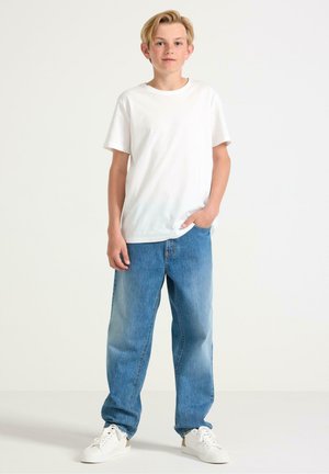 Vit kortärmad t-shirt, ljusblå jeans och vita sneakers. Jeansarna är löst sittande med en blekt look och klassisk femficksdesign.