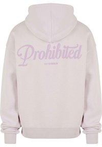 Hoodie rose clair en tissu doux ; présente un grand texte "Interdit" en violet pastel au dos, avec des poignets et un ourlet côtelés.