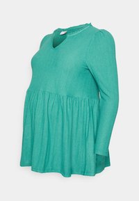 Top de maternidade malha verde com colarinho franzido, mangas longas e linha de cintura larga. Tecido texturizado com padrões subtis.