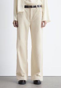 Beige corduroy wide-leg pants with a smooth texture, featuring a black leather belt and side pockets. Flat front with a relaxed fit.