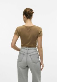 Brun kortærmet t-shirt parret med højtsiddende lysegrå jeans. T-shirten har en rund halsudskæring og en tætsiddende pasform.