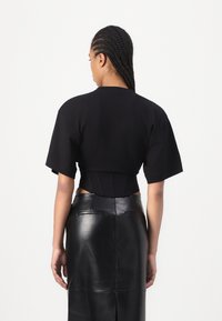 Černé zkrácené tričko s krátkým rukávem, přiléhavý střih v pase. Kombinováno s elegantní černou koženou sukní s rozparkem vzadu.