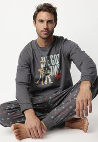 Camisa gris de manga larga con un estampado gráfico de personajes, combinada con pantalones de pijama con patrones de estrellas y cohetes.