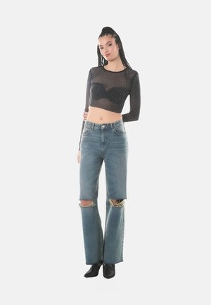 Top corto in rete nera con maniche lunghe e pois, abbinato a jeans a vita alta blu chiaro con orli strappati e vestibilità comoda.