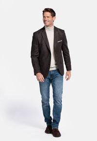 Bruine wollen blazer met notch lapels, gecombineerd met een lichtgrijze coltrui, blauwe jeans en donkerbruine suède schoenen. Accent pochet zichtbaar.