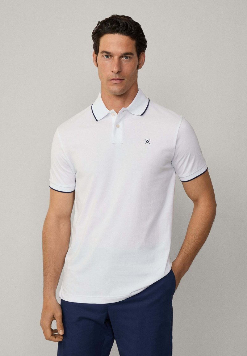 Polo shirt bianco con colletto e dettagli delle maniche blu navy. Presenta una pattina con tre bottoni e un piccolo logo sul lato sinistro del petto.