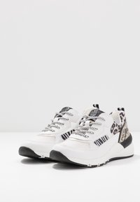 Bílé a černé tenisky s kombinovanými zvířecími potisky, černo-bílé pruhované tkaničky a robustní podrážkou na bílém povrchu.