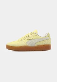 Gule semskede sneakers med en hvit skinnside stripe, gummisåle og brodert logo på tungen og hælen. Lav profil.