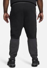 Schwarze und graue Sweatpants mit schmal zulaufendem Design, versehen mit einer glatten Textur und einem elastischen Bund. Reflektierende Nähte in der Nähe des Knöchels.