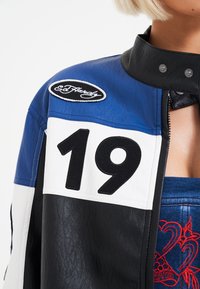 Giacca di pelle con pannelli neri, bianchi e blu, caratterizzata da un grande ricamo "19" e un logo Ed Hardy sulla spalla.