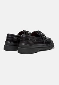 Black leather shoes with a low profile, round toe, and textured finish. Features thick rubber soles and traditional lace-up design.
