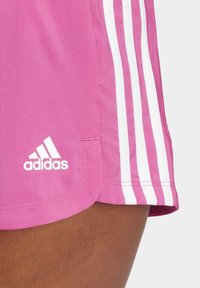 Pantalones cortos deportivos rosa con diseño de tres rayas blancas en los lados y un logotipo blanco de Adidas en el dobladillo. Hechos de un material ligero y transpirable.