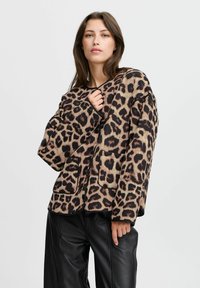 Giacca a pois leopardati in beige, con dettagli neri, due tasche frontali e una vestibilità comoda. Realizzata in un morbido tessuto testurizzato.