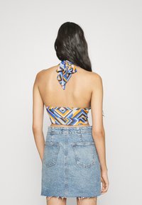 Top halter colorido com padrões geométricos em azul, laranja e cinza, combinado com uma saia mini de denim com bainha desfiada e bolsos traseiros.