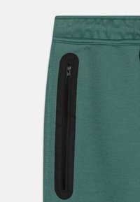 Green jogger pants with a smooth texture, featuring a black zippered pocket on the side and elastic waistband for comfort.