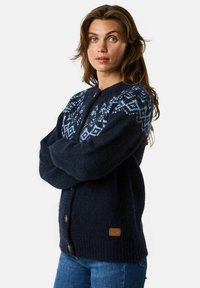 Marineblauwe gebreide cardigan met geometrische lichtblauwe patronen op de schouders, houten knopen en een gestructureerde stof. Voorzien van een logo-patch aan de zoom.