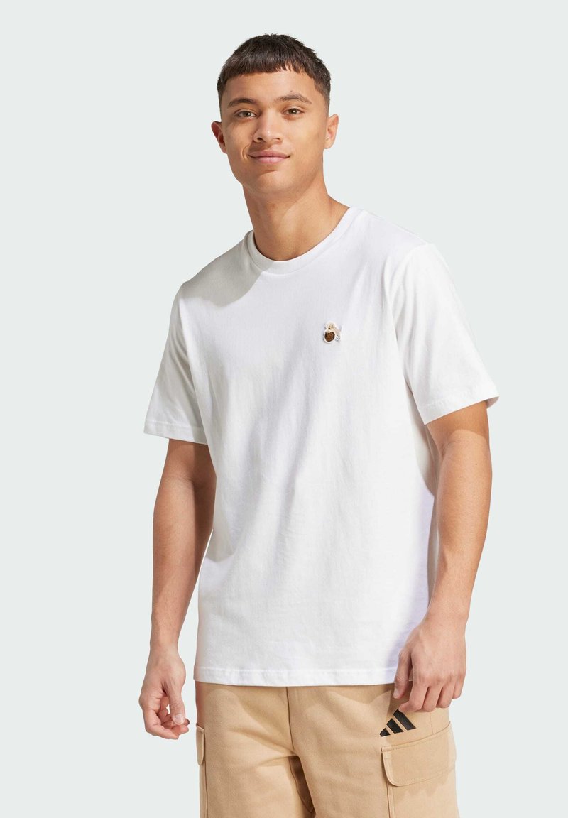 Hvid bomulds t-shirt med rund halsudskæring, der har et lille brunt bjørnesøm på brystet, korte ærmer og en afslappet pasform.