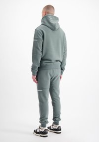 Grijze hoodie en bijpassende joggingbroek, van katoenmix, textuurstof, met een logo op de arm, gedragen met zwart-witte sneakers.