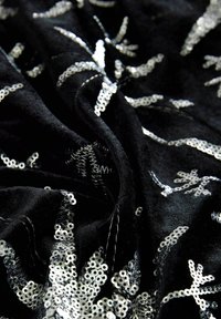 Fekete bársonyszövet ezüst flitteres virágos hímzéssel, bemutatva a redőket és a részletes textúrát.