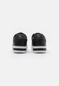 Zapatillas de cuero negras con suelas blancas, que cuentan con un logo dorado en el talón y una franja negra a lo largo de la entresuela. Textura suave, diseño de bajo perfil.