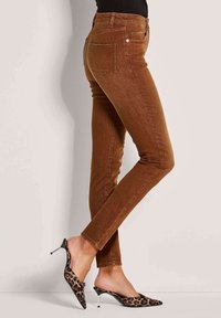 Bruine denim skinny jeans met hoge taille, voorzien van achterzakken en een slim fit, gecombineerd met zwart en luipaardmotief hakken.