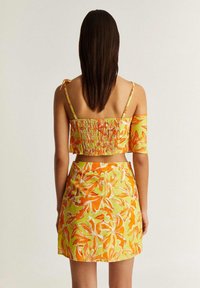 Ensemble à deux pièces comprenant un crop top smocké avec des bretelles et un détail décolleté, assorti d'une mini jupe, le tout dans des motifs floraux vibrants.