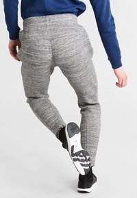 Grå atletiska joggers med ett texturerat mönster, elastisk midja och slim fit, parat med svarta sneakers med vita sulor.