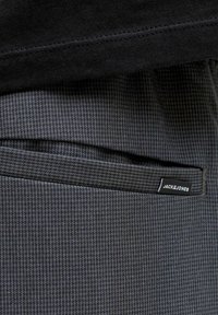 Tmavošedé nohavice z textúrovaného materiálu s čiernym pásom a malou čiernou značkovou nálepkou Jack & Jones na okraji vrecka.