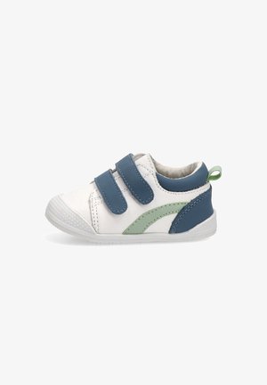 Zapato blanco para bebé con correas de velcro azules, detalles en azul y verde, y una lengüeta para tirar en el talón, mostrado de perfil sobre un fondo blanco.