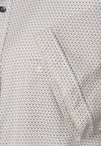 Korte mouw shirt van een lichte stof met een geometrisch patroon van blauwe en bruine rechthoeken op een crèmekleurige achtergrond.