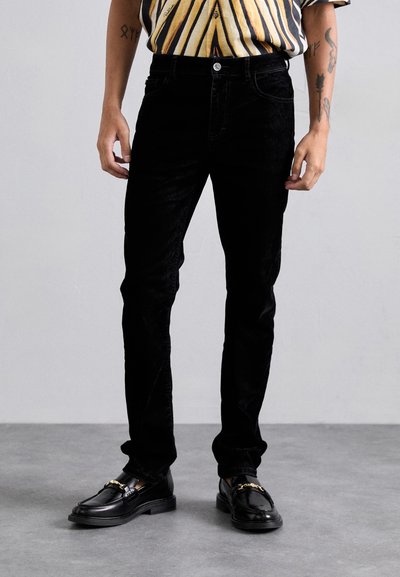 Pantaloni negri din corduroy cu un design slim fit, având o închidere cu nasture și buzunare frontale, asortați cu loafers negri.