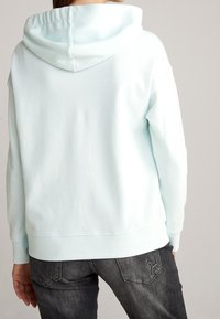 Light blue hoodie with a drawstring hood, ribbed cuffs, and hem. Features a smooth texture and a relaxed fit, paired with dark denim jeans.
