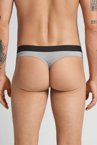 Männliches Modell in grauen und schwarzen Tieferchnitten, von hinten gezeigt, mit sichtbaren Tätowierungen auf beiden Armen vor einem einfarbigen Hintergrund.