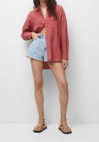 Rode linnen overhemd met knopen aan de voorkant, gecombineerd met lichtblauwe denim shorts met rafelige randen. Neutrale sandalen met een eenvoudig bandontwerp.