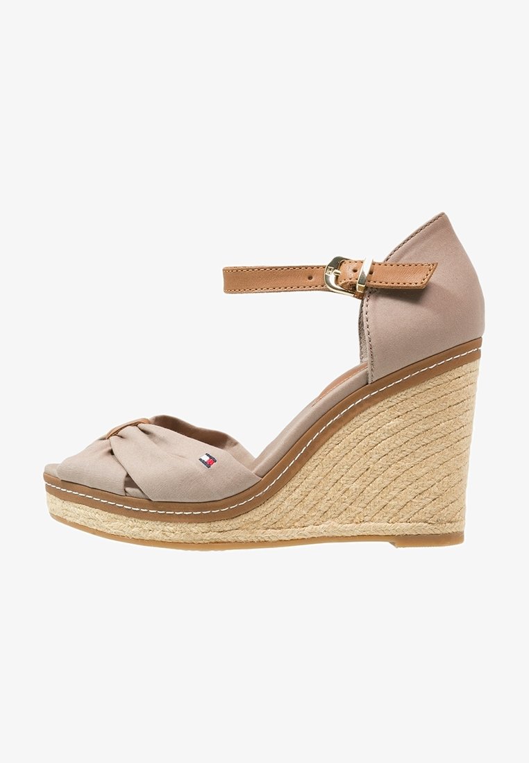 Sandales compensées beiges avec une lanière en tissu nouée sur le bout, une lanière à la cheville couleur beige et un talon enveloppé de jute avec des coutures blanches le long du bord.
