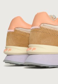Un paio di sneaker in suede beige, con dettagli in pelle pesca e suole lavanda, viste da dietro su uno sfondo neutro.