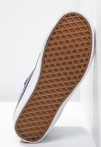 Semelle de basket bleue avec une surface texturée en caoutchouc, présentant une accroche à motif de losange et une bordure blanche le long du côté.