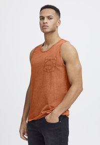Hnědý tank top s kulatým výstřihem, detaily kapsy a kartáčovanou texturou. Nosit přes tmavé džíny s volným střihem.