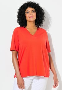T-shirt rosso a collo a V con maniche corte, realizzato in un tessuto morbido. Presenta delle fessure laterali per facilitare i movimenti. Abbinato a pantaloni bianchi.