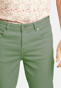 Pantalones de denim verde con una textura suave, que presentan un clásico diseño de cinco bolsillos y un discreto botón metálico en la cintura.