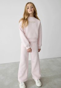 Ljusrosa sweatshirt och byxset, med en kortad design, ribbad mudd och "BAKER" i guldtext på bröstet. Mjuk textur.