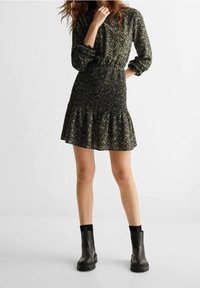 Black floral dress with long sleeves, smocked bodice, and tiered skirt. Paired with black ankle boots featuring thick soles.