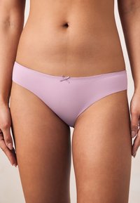 Hele lilla bikiinipüksid, millel on sile pind, lihtne disain ja väike lipsuke vöökohal.