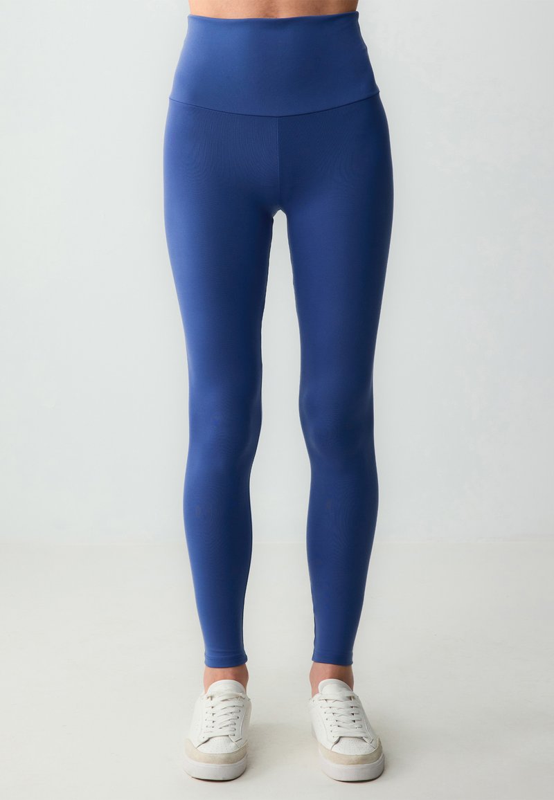 Marineblauwe leggings met een hoge tailleband, gemaakt van rekbare stof. Gladde textuur met een aansluitend ontwerp, gecombineerd met witte sneakers.