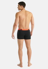 Svarta boxershorts med en röd elastisk midjeresår med logotypdetaljer. Materialet verkar vara stretchigt och bekvämt, utformat för sportklädsel.