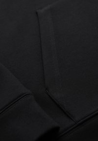 Gros plan d'un tissu noir avec des détails visibles de couture sur une couture pliée et un poignet de vêtement.