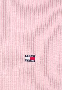 Roosa ribatatud kampsun, millel on kangast münt "TOMMY JEANS" tekstiga ja väike graafika sinises, valges ja punases.