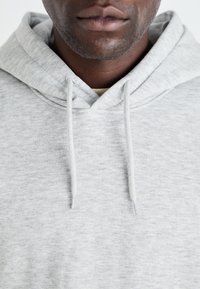 Grijze hoodie van zacht materiaal, met een trekkoord in de capuchon en ribbelboord bij de hals, met een subtiele gemêleerde textuur.