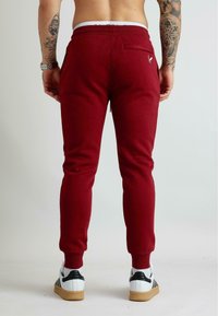 Czerwone spodnie dresowe wykonane z bawełnianej mieszanki, zwężany krój, elastyczny pas, tylna kieszeń, ściągacze przy nogawkach, zestawione z białymi tenisówkami.