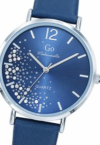 Montre en quartz bleue avec un boîtier en métal argenté, un bracelet en cuir texturé bleu et des accents en cristal créant un effet scintillant sur le cadran.